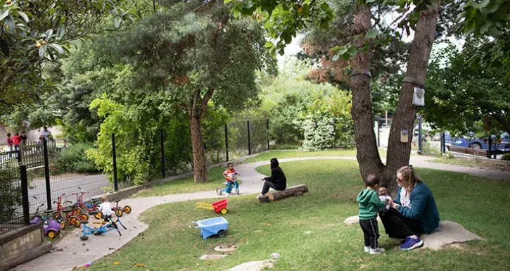 Dans le jardin de la crèche Manufacture, à Nantes, une éducatrice joue avec un enfant. L'environnement est très vert, avec pelouse et arbres. 