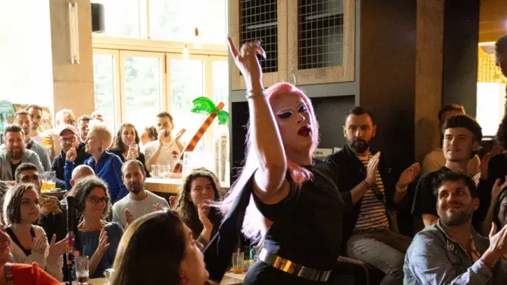 Dans un bar, une drag-queen aux cheveux rose danse.