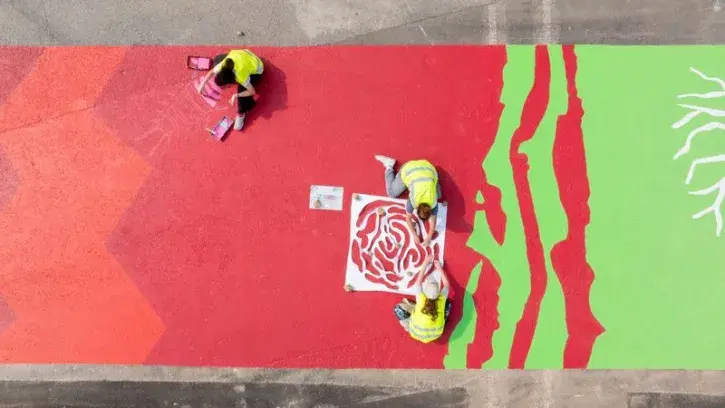 Des personnes peignent sur le sol de la place de la Petite-Hollande une fresque colorée symbolisant la biodiversité.
