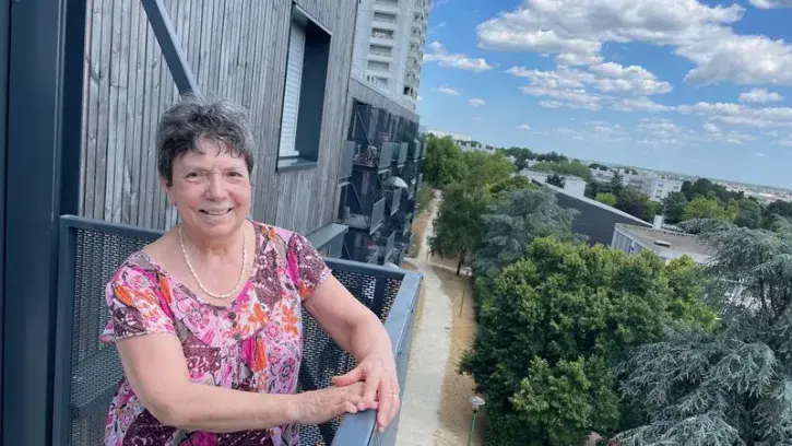 Une habitante appuyée à la rambarde de son balcon, dans un quartier rénové en 2025.