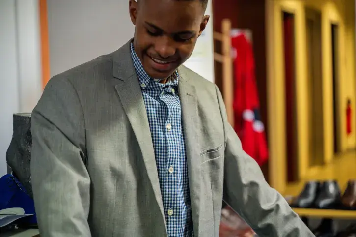 Un jeune homme essai un costume gris et une chemise bleue avec le sourire