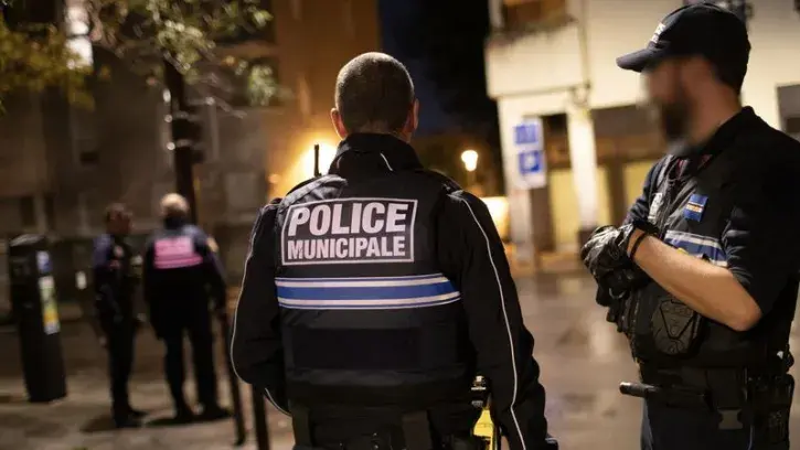 Place de la Galarne. La place, plongée dans l'obscurité, est calme. Légèrement à l'écart, un individu, capuche sur la tête, observe les allées et venues des forces de l'ordre. Équipés de lampes torches, les policiers fouillent les parterres de fleurs. Ces