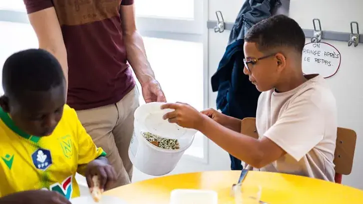 Youssef vide les restes de son assiette dans le seau qui permettra de mesurer le gaspillage du repas végétarien du jour de la cantine de l'école Joséphine Baker à Nantes © Garance Wester pour Nantes Métropole